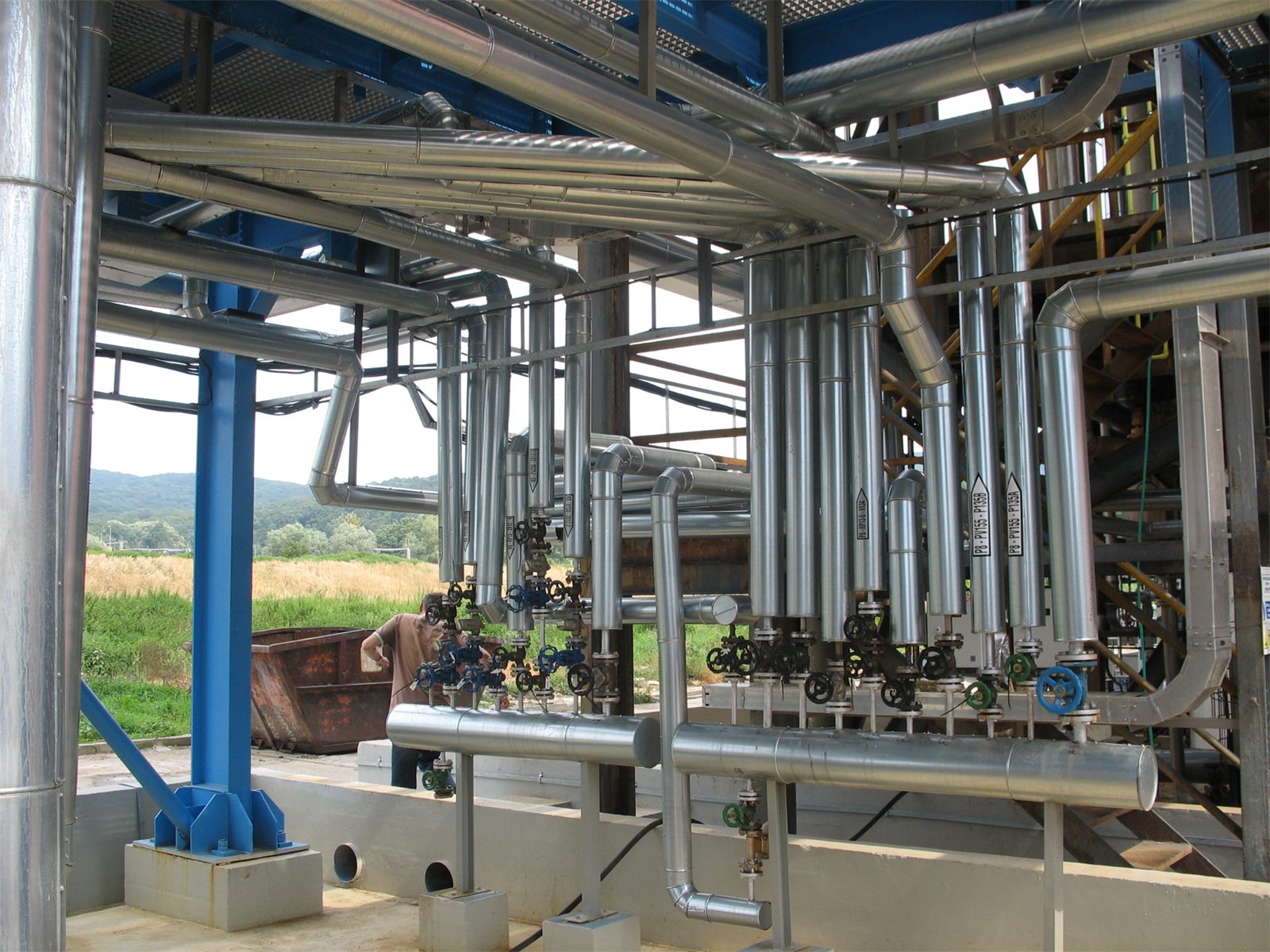 Insulated and stainless process piping with valves under a blue steel structure